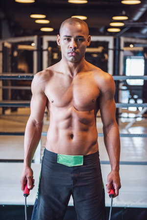 Handsome young boxer is holding a skipping rope and looking at camera while training in gymの写真素材