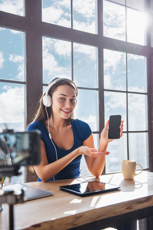 Young beautiful girl blogger working in office while shooting at camera listens to music in headphonesの写真素材