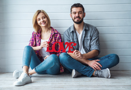 Young happy loving couple sitting on floor and holding sign "Love", smiling at cameraの写真素材