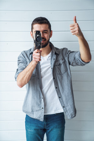 Young emotional man while shooting with old camera on light backgroundの写真素材