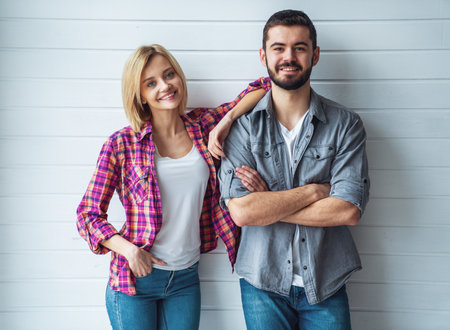 Portrait of young cheerful loving couple smiling looking at camera and hugging each other on light backgroundの写真素材