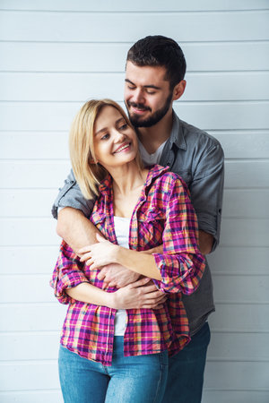 Portrait of young cheerful loving couple smiling looking at camera and hugging each other on light backgroundの写真素材