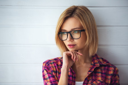 Portrait of a young beautiful blonde girl on a light background with glassesの写真素材