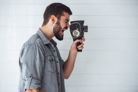 Young emotional man while shooting with old camera on light backgroundの写真素材