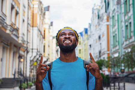 A young man rejoices raising his fingers up while walking the streets of the bridge with a backpackの写真素材