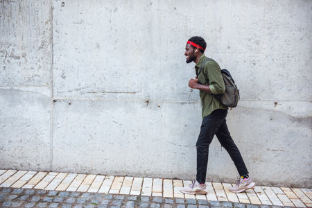 A young man walks on the sidewalk while walking the streets of a bridge with a backpack near a large wallの写真素材