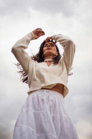 Retro style. Full-length portrait of a young beautiful girl with chic black hair in a white dress against the sky and clouds.の写真素材