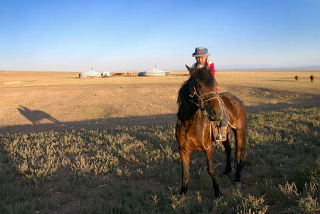 A little girl on a horse in Mongolian steppe, yurts on the backgroundのeditorial素材