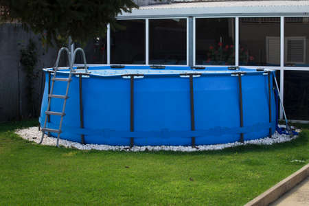 Blue swimming pool with ladder on green grass in the backyard of the houseの写真素材