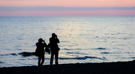couple silhouette photographing the sunset on the beachの写真素材