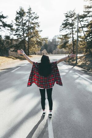 Young happy girl in red wearing a checkered shirt walks on the middle of a road. Wide-open shirt. Awesome atmosphere, Spring timeの写真素材