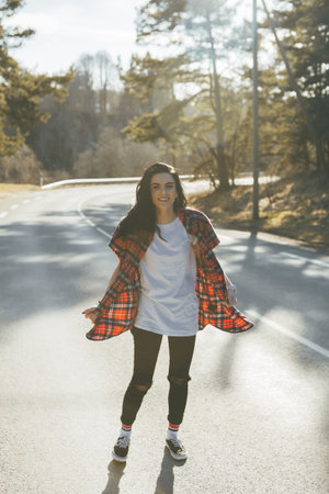 Young hipster girl is standing on the middle of road at the forest. Awesome atmosphere, spring,...