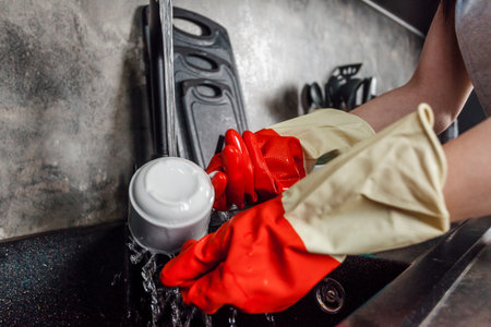 close up of the hands of a housewife in gloves washIng dishes in a modern kitchen.