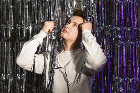 Portrait of a young man in white sweater and creative decoration on the face standing between shiny...