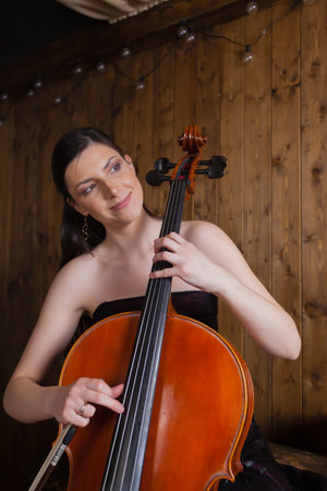 A creative cellist is playing the cello against a wooden background.の写真素材