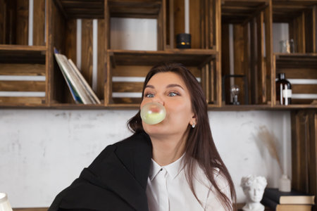 The concept of female beauty. Portrait of a fashionable young girl in classic clothes blowing bubble gum, posing over vintage retro styled background. Fashion style. studio shot.の写真素材