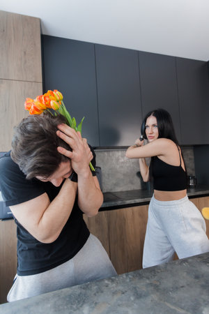 A man came to his girlfriend with flowers, but she met him with a frying pan. family quarrel.  Infidelity and trust issues. Relationships crisis, conflict.の写真素材