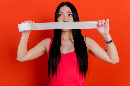 Close-up portrait of charming girl holding white paper tape over isolated background.の写真素材