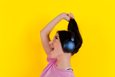 Portrait of a charming, joyful music lover holding, pulling pigtails or hair in her hands against a bright yellow background. Emotions, lifestyle, leisure, music, and dance concept.の写真素材