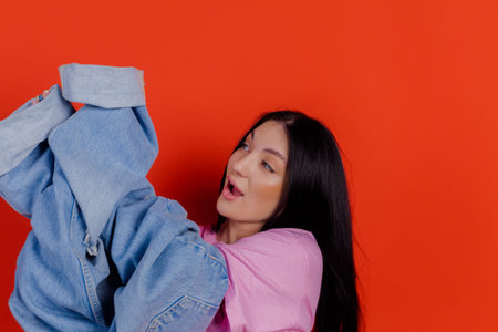 Close-up portrait of charming joyful beautiful girl posing with jeans against a bright red background. People emotions, lifestyle leisure, creative fashion concept.の写真素材