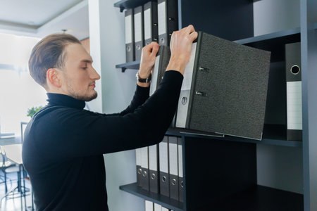 The office worker takes a stack of folders from the shelves.