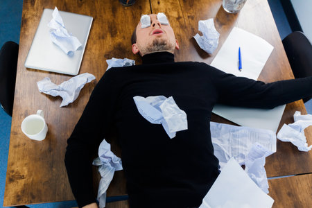 Unhappy frustrated businessman going crazy without any ideas, crumpled paper around on table. Concept of no idea.の写真素材