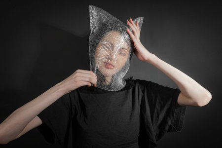 Portrait of a poor skinny girl in black crumpled clothes with a plastic bag on her head. isolated on...