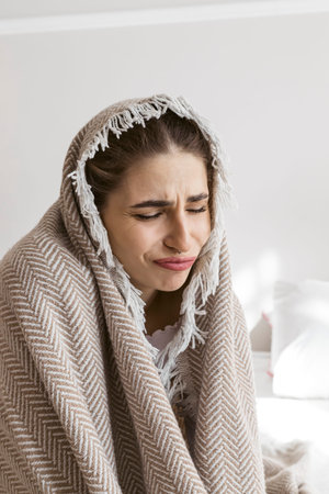Portrait of a beautiful girl sitting on a bed and wrapped in a blanket due to the cold. Freezing....