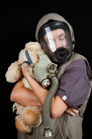 A portrait of a sad girl and a plush toy hugging each other while wearing gas masks, on an isolated black background. Concept of Protecting each other, nature and air pollution problems.の写真素材