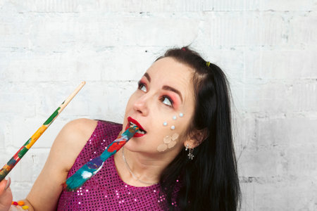 Portrait of a dark-haired woman with a creative face decorations, holding a painting brush with...