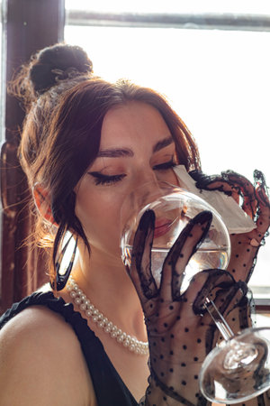 Beautiful, gorgeous and elegant girl in a black dress and Mesh Sheer gloves on her hands, drinking water. Concept of elegance and sophistication. Formal or upscale event.の写真素材