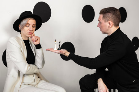 A man holds a black and white chess piece in his hand, offering a woman, his opponent a choice of which side to play.の写真素材