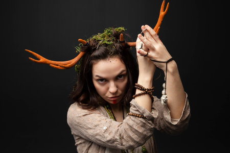 A portrait of a female druid or shaman with horns, holding ritual talismans in her hands on a black isolated background.Shamanic practices,Spiritual rituals,Pagan beliefs,Nature worship,Mystical.の写真素材