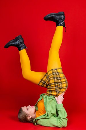A cute beautiful girl in a green and yellow clothes posing against an isolated red background. Lying...