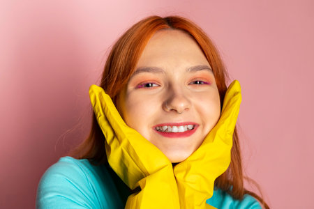A red-haired girl wearing a chemical protection gloves and smiling on an isolated pink background. Emphasizing safety regulations.の写真素材