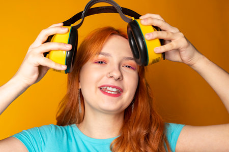 A red-haired girl wearing a hearing protection and smiling on an isolated orange background.の写真素材