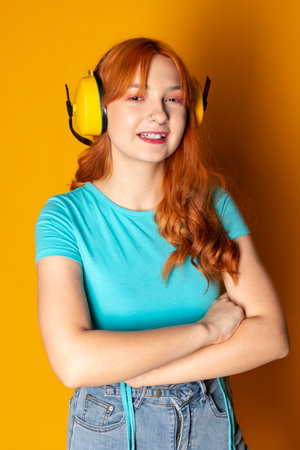 A red-haired girl wearing a hearing protection and smiling on an isolated orange background.の写真素材
