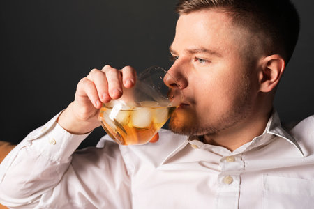 An attractive young successful man in a white shirt drinks whiskey with ice. A businessman having a break after work.の写真素材