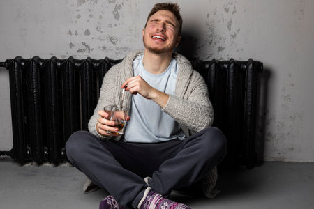 Insanely laughing young man sitting on a floor with a sigarette and alcohol in his hands.の写真素材