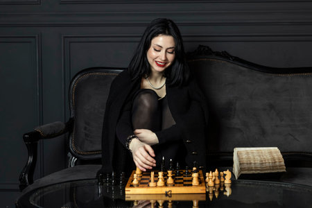 Portrait of a beautiful, elegant girl in black with bright matte red lipstick, sits behind a wooden...