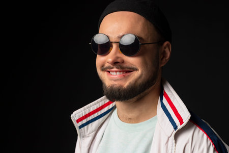 A young, tough guy from the streets dressed in a tracksuit and round sunglasses, posing, isolated on...