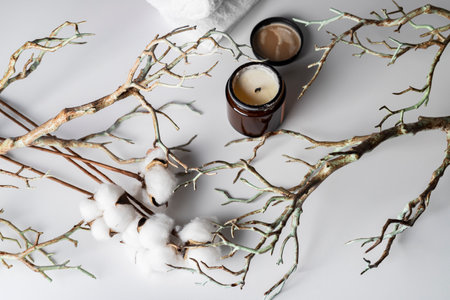 Blooming cotton branch, tree branches, aromatic candle, and a rolled-up white towel, isolated on a white background. A spa day concept, relaxation, self-care, natural beauty, or organic products.の写真素材