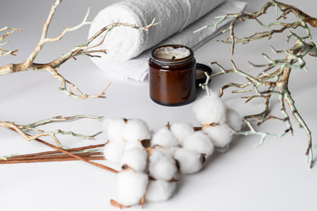 Blooming cotton branch, tree branches, aromatic candle, and a rolled-up white towel, isolated on a white background. A spa day concept, relaxation, self-care, natural beauty, or organic products.の写真素材