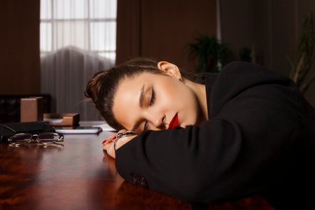 A beautiful businesswoman or psychologist, formally dressed, is laying her head down on a table with closed eyes, looking tired after work.の写真素材