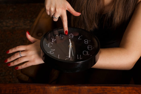 A young and attractive woman in an elegant black dress with long loose hair points to watch with her...