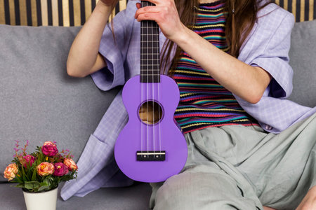 A pretty hippie girl in a striped t-shirt and wide loose pants tangled her hair in an ukulele.の写真素材