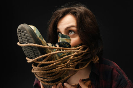 Girl with a shoe tied to her face with a rope, blocking the ability to breathe normally. Isolated on a black background. Concept of suffocation and environment pollution, bad air.の写真素材