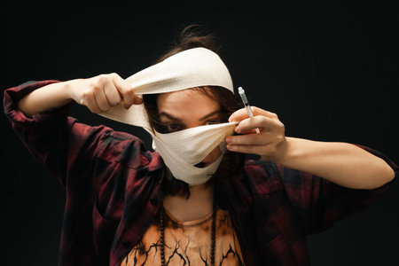 A girl with almost completely bandaged face who is removing the bandages. Isolated on a black background. Concept of healing and recovery.の写真素材