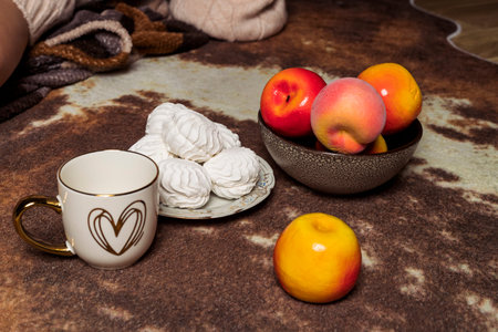 A cup of tea or coffee with sweets and fruit are lying in a cozy atmosphere.