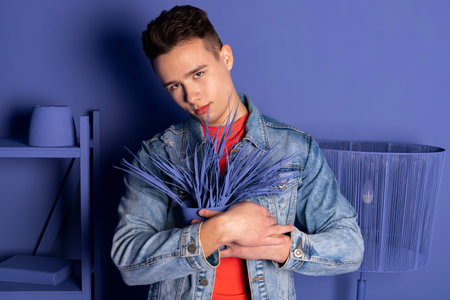 Portrait of a handsome young man in denim clothes posing in a room where everything is blue or purple, a room that is completely painted in one color.の写真素材